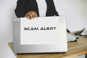 Un homme d'affaires tenant un panneau d'alerte aux escroqueries sur un ordinateur portable, mettant en garde contre la fraude en ligne.