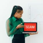 Une femme en vert pointe un ordinateur portable affichant le signe « ARNAQUE », soulignant la sensibilisation aux escroqueries en ligne.